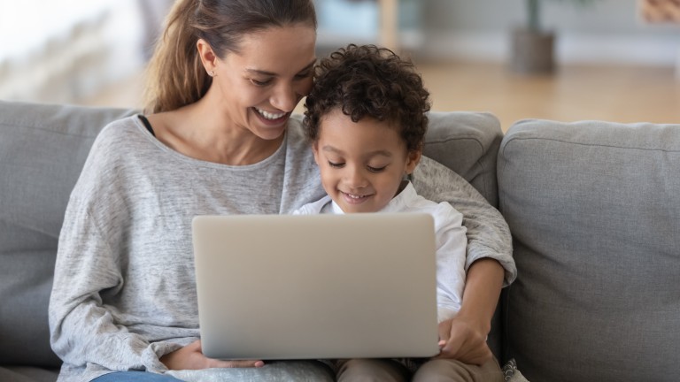 Smiling mother with African American son using laptop close up, happy mum and preschool child sitting on sofa at home, watching cartoons online or play video game, family having fun.